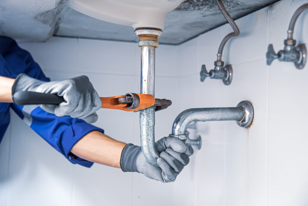 Technician Plumbers in Ludlow using a wrench to repair a water pipe under the sink. Concept of maintenance, fix water plumbing leaks, replace the kitchen sink drain, cleaning clogged pipes is dirty or rusty.